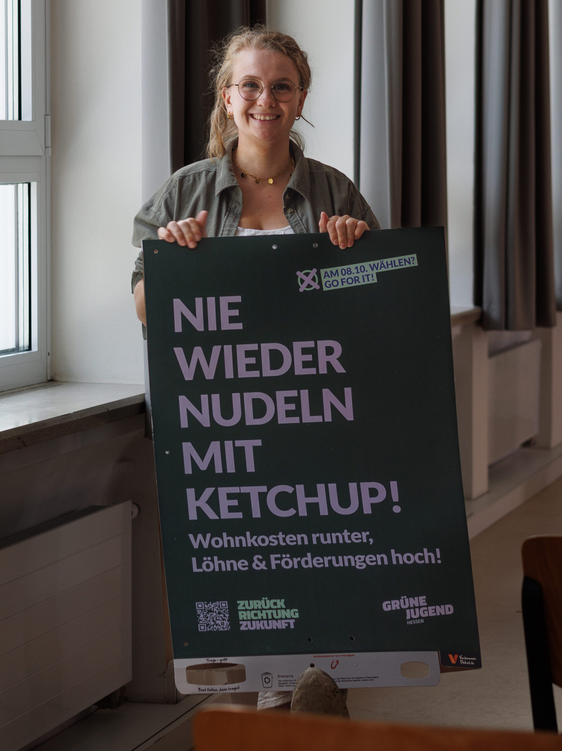 Ein Bild von unserer Landesgeschäftsführerin Nora. Auf dem Bild hält sie ein Plakat aus dem Landtagswahlkampf hoch. Auf dem steht "Nie wieder Nudeln mit Ketchup". 